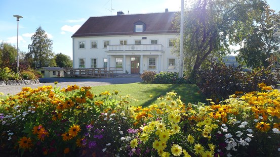 Foto av skolhuset med blommor i förgrunden.