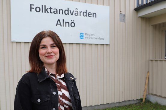 Elin står utanför entrén till folktandvården Alnö, hon är glad tittar in i kameran.