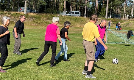 Seniorer spelar gåfotboll utomhus på en gräsyta.