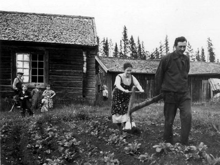 Svartvitt fotografi med en jordbrukarfamilj framför ett torp, från början av 1900-talet.