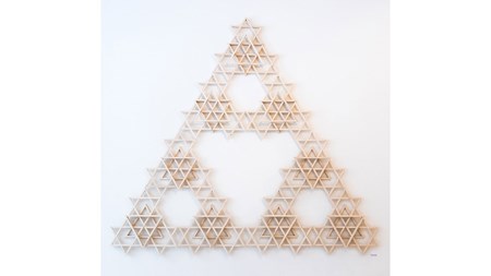 På vit vägg sitter många mindre trianglar av trä i form av en stor triangel. Tillsammans formar de mönster, större trianglar