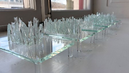 Sex stycken små sängar av glas står på rad, på dem är krossat glas i olika formationer. 