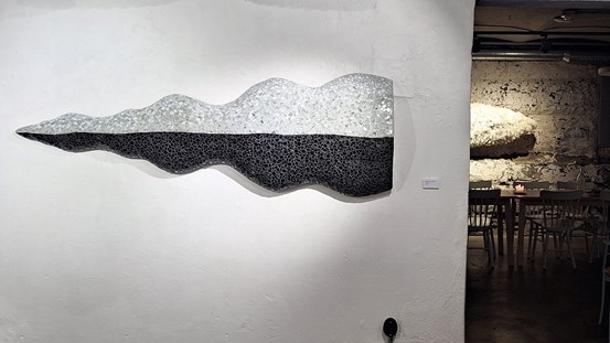 Vägghängt, spetsliknande verk med vågiga långsidor. Spetsen åt vänster,  kortsidan platt. Nedre halvan mörk och övre ljus. 
