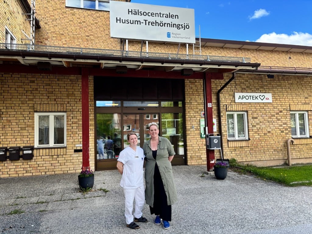 alt='Två personer står framför hälsocentralens entré'
