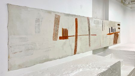 En rektangulär, liggande målning. Den långa duken hänger på en vit vägg. På en gråvit bakgrund syns olika former i brunt, rött och svart. 