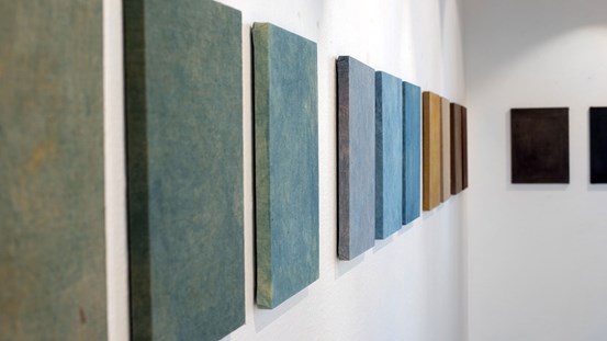 Vy över utställning. Vägg med många målningar på rad i olika färgtoner.