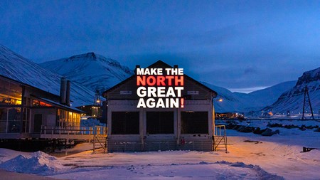 Foto på ett hus i ett snöigt samhälle kvällstid i ett gulaktigt sken från lampor. Snöiga berg och en molnig himmel syns i den blåtonade bakgrunden. Mitt i bilden står texten "Make the North Great Again" i vitt och rött. 