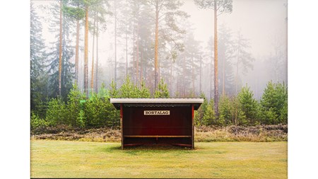 Foto av en avbytarbänk med skylt "Bortalag" vid kanten av en fotbollsplan framför skog. 