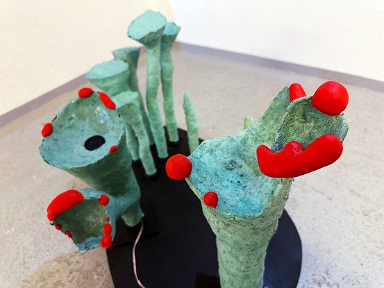 Flera gröna, strutformade skulpturer sedda snett uppifrån. Några har röda runda former längst upp.