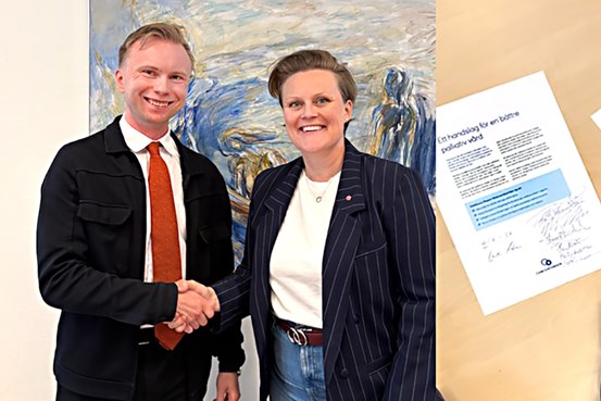 Två personer i ett handslag framför en vägg, bredvid ligger ett signerat kontrakt