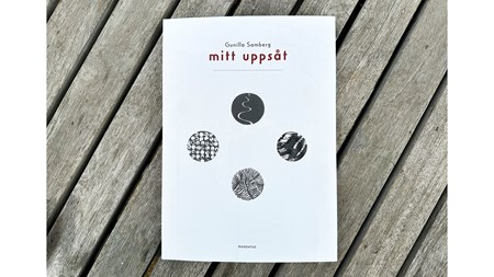 Foto av en bok liggandes på ett utegolv av trä. 