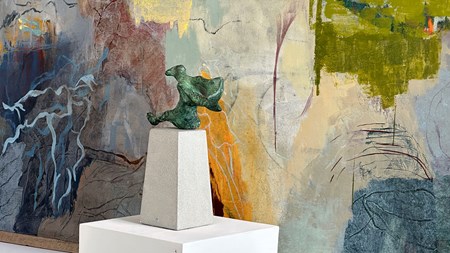 En ärggrön bronsskulptur på ett podium. Bakom, en målning, ett abstraherat landskap. 