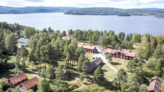 Landskapsvy, röda hus med vita knutar i ett grönt landskap. Längre bort syns vatten och skog. 