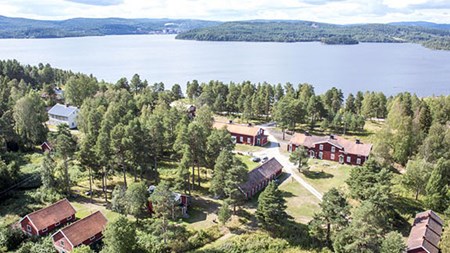 Landskapsvy, röda hus med vita knutar i ett grönt landskap. Längre bort syns vatten och skog. 