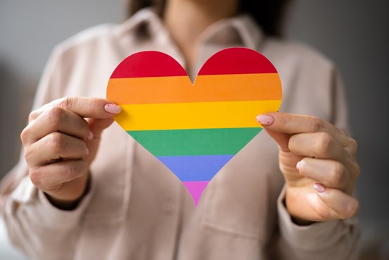 Person som håller upp ett regnbågsfärgat hjärta av papper
