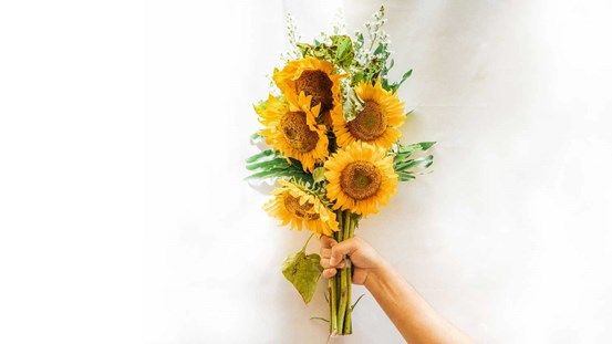 En hand som håller i en bukett med blommor, främst solrosor.