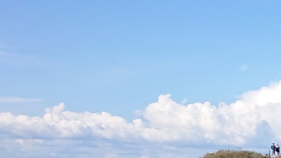 En blå himmel med moln. Längst ner till höger ett par vid en yta gräs. 