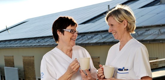 Två sjukvårdspersonal dricker kaffe i solen.
