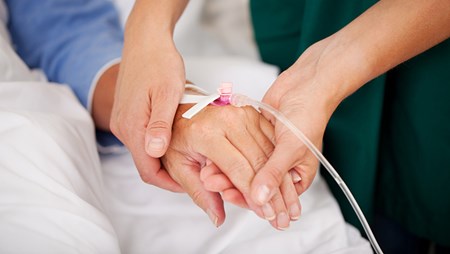 Sjuksköterska håller en patients hand som har en infart. 
