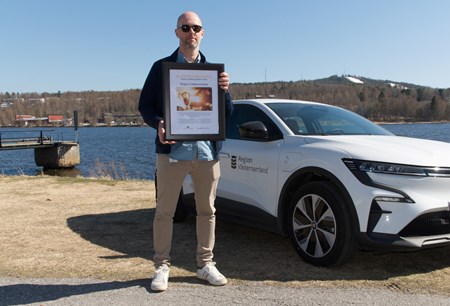 Mattias Almqvist står framför en av Region Västernorrlands bilar och visar upp ett diplom
