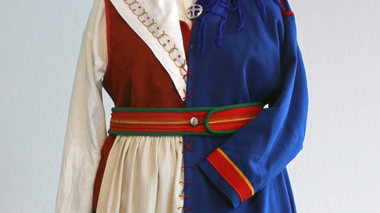 En traditionell tornedalsk folkdräkt och en samisk examenskolt i kornblått, förenade med stora, framträdande röda stygn.