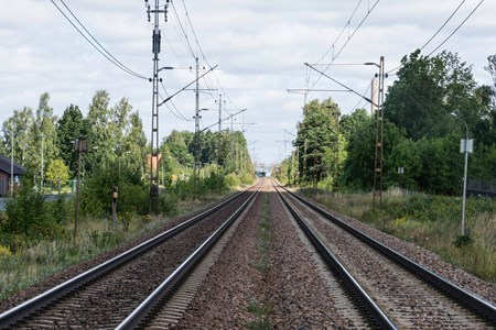 Dubbla järnvägsspår med grönskande skog runt om.