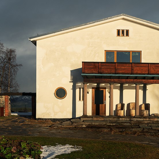 En gulaktig husfasad i solsken. Himlen i bakgrunden är mörk. 