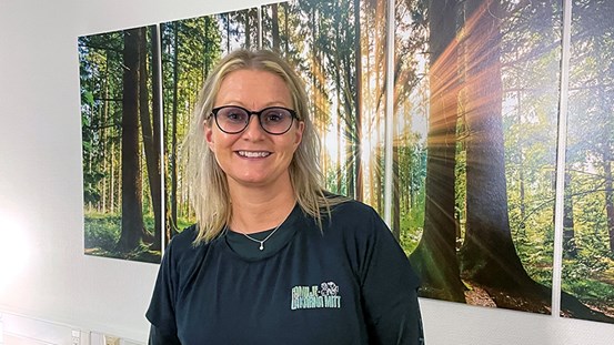 Porträttbild på Carola Petterson, i bakgrunden en tavla med skog