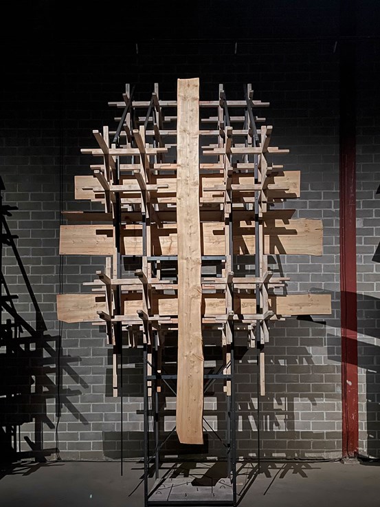 En hög träkonstruktion framför en grå tegelvägg. 