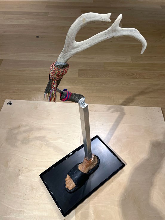 En skulptur bestående av snidad fot i körsbärsträ, Lidl-toffla, renhorn och vävda band.