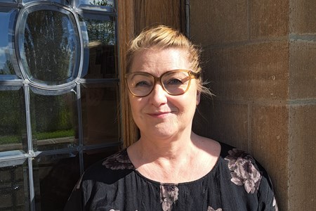 Porträttbild av läraren Kristina Ståhlnacke som står utomhus vid folkhögskolans entrédörr.