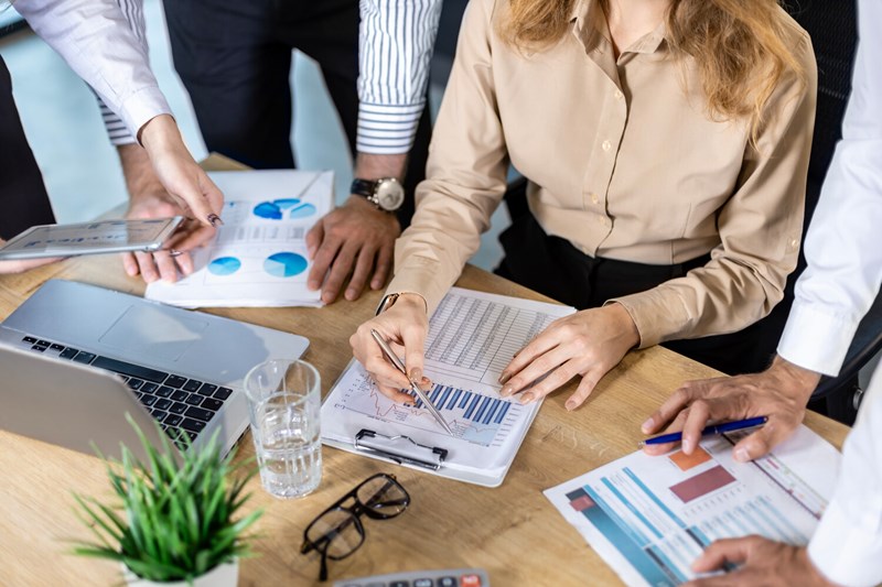 Tre personer sitt runt ett bord med massa papper på. De analyserar statistik.