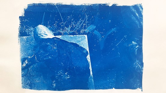 Diffus bild i blå toner, person med ryggen mot betraktaren, hukande med boxhandskar framför en vit yta. Djupblå bakgrund. 