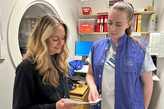 Två kvinnor varav en i sjukvårdskläder samtalar och tittar på ett papper.