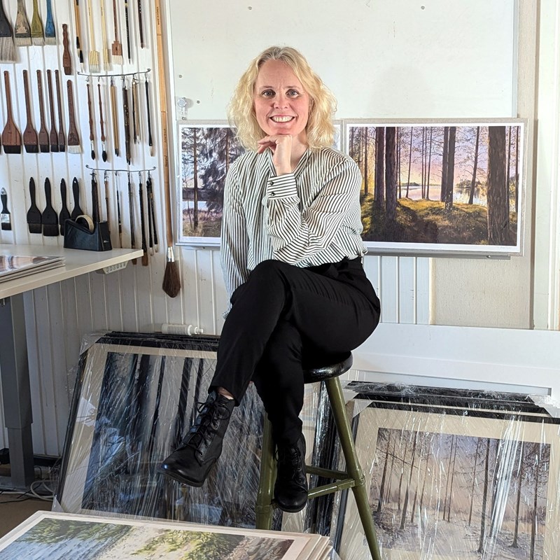 Anita Rosvall omgiven av tavlor i en ateljé