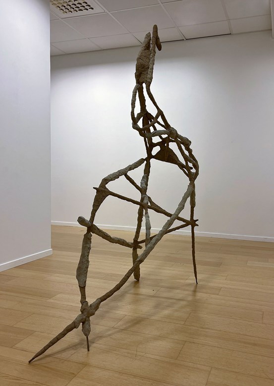 En skulptur av en tunn pinnliknande konstruktion överdragen med lera.