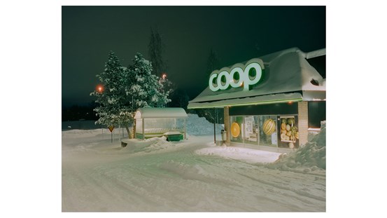 Foto. Omgiven av snö, en Coop-butik i ett vintermörker, upplyst av gatlampor, Coop-skylten på tak och butiksbelysning. 