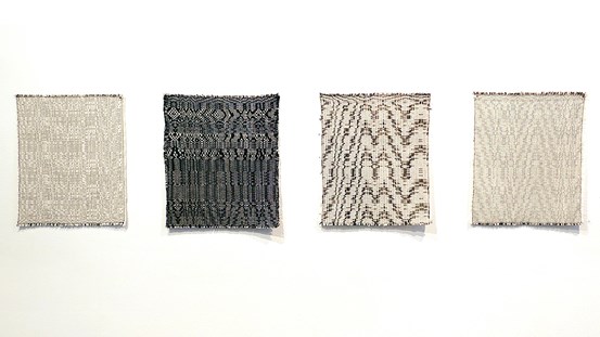 Fyra nästan kvadratiska vävar i beige, ljusbrunt och svart häger på rad på en vit vägg. 