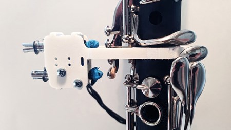 Närbild av den modifierade klarinetten. Bland kromade klaffar sitter en vit tillbyggnad fastsatt. Det är magnetspolar inneslutna i en 3D-tryckt hållare. 
