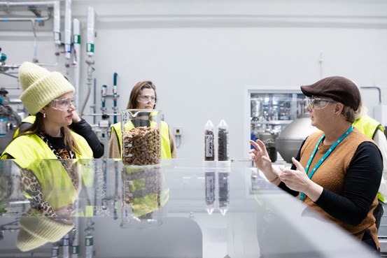 Tre personer i gula västar runt ett blankt bord. 