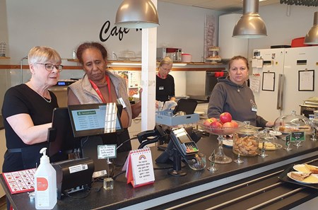 Fyra kvinnor står bakom cafédisken varav två tittar på kassaapparaten. 