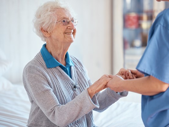 Äldre kvinna håller hand med vårdpersonal.