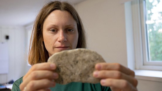 Jenny Käll, AIRY-stipendiet 2021, håller fram ett prov där sand bränts in i lera och bildat en form av glasyr.