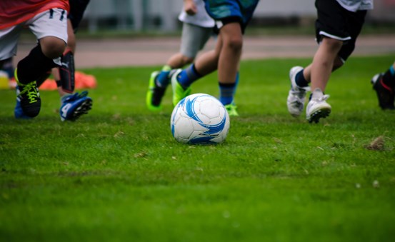 Barn som spelar fotboll på gräsplan.