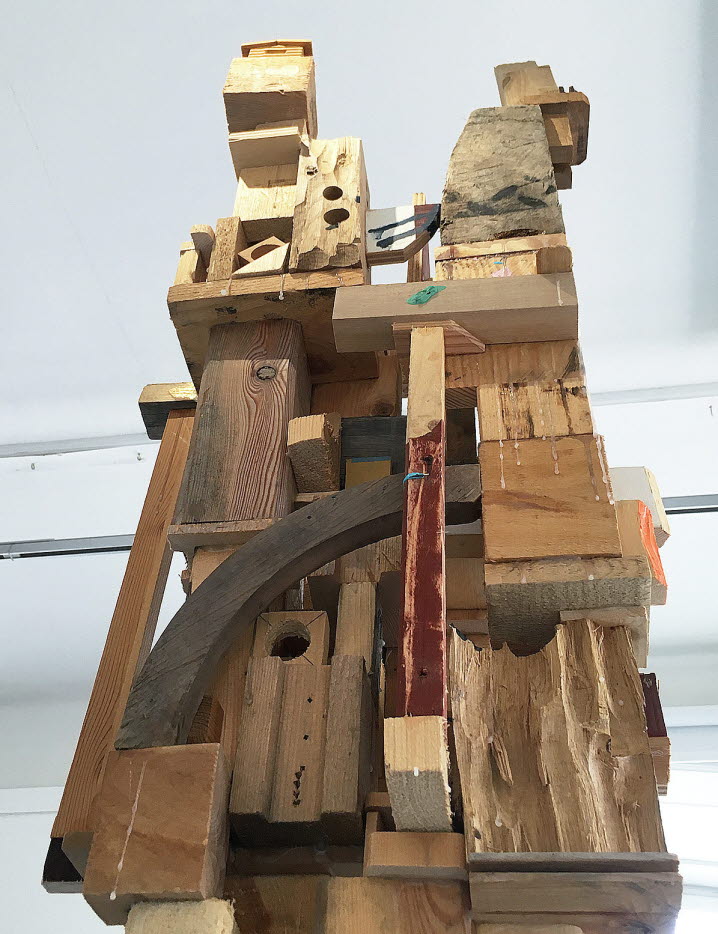En skulptur av återvunna träbitar bildar ett trätorn som reser sig mot taket.