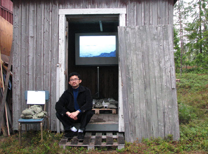 Suchart Wannaset sitter i dörröppningen till det lilla hus vari han visar sin installation och sitt videoverk under Blånagla Artfest.