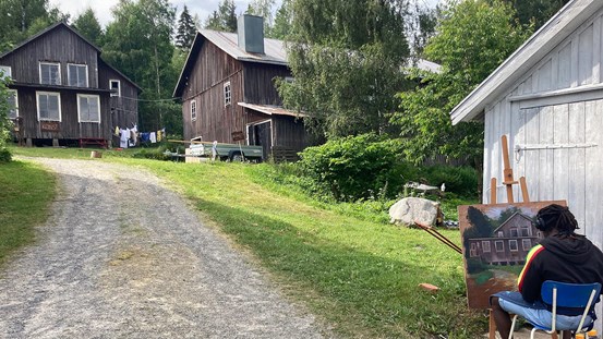 Fotografi som visar den gamla skofabriken i Vännersta. En konstnär sitter i nedre högra hörnet och målar av byggnaden.