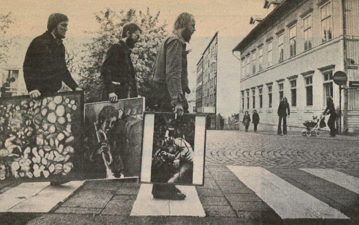 Svartvitt pressfoto från 1975 där tre män vandrar över gatan med varsin tavla i handen. Det är gruppen REX, med Lars längst fram, de parafraserar ett legendariskt skivomslag, på väg till utställningen i Örnsköldsvik.