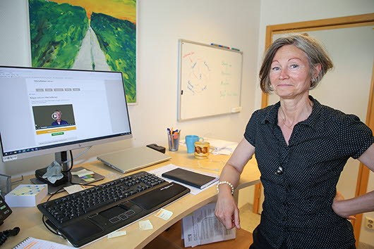 Anne-Li i halvfigur står bredvid sin dator och lutar ena armen mot bordsskivan. Anne-Li har en kortärmad svart blus.