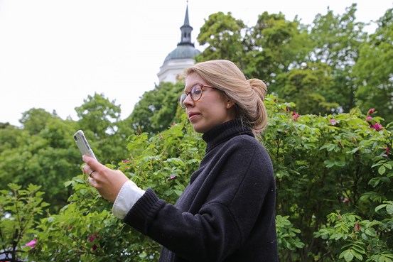 Antonia tittar på sin mobiltelefon, kyrkan i Härnösand syns suddigt i bakgrunden.